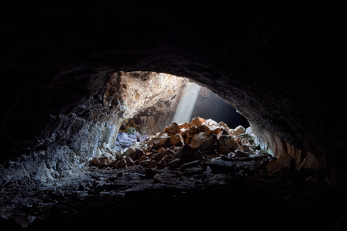 The absolute darkness of the lava tube gives way to a small glow of light from a small opening in the top of the tube created...